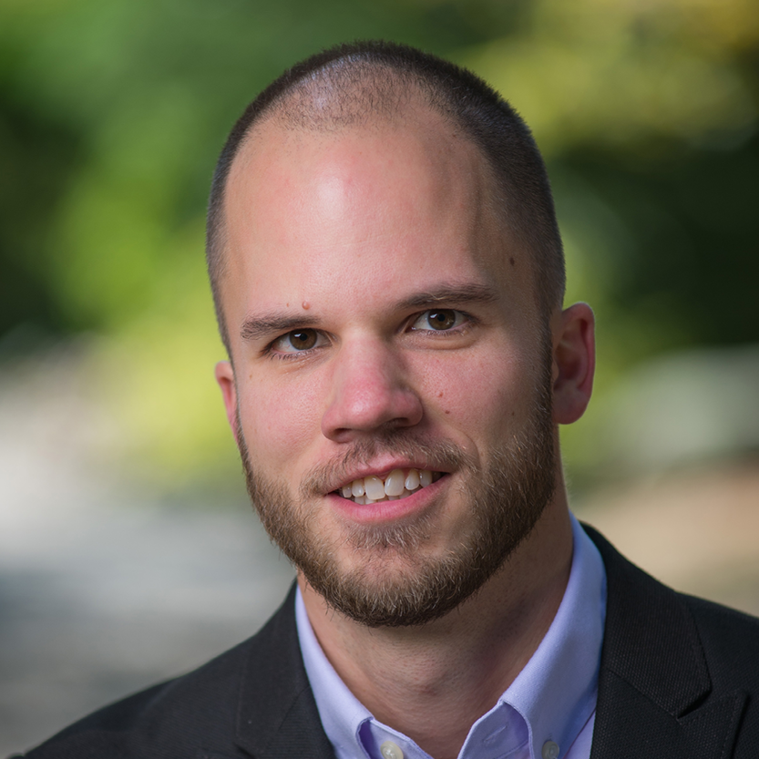 A portrait picture of Evan Hammer. He is a white man in his mid-20s. He has brown eyes and is wearing a black blazer.