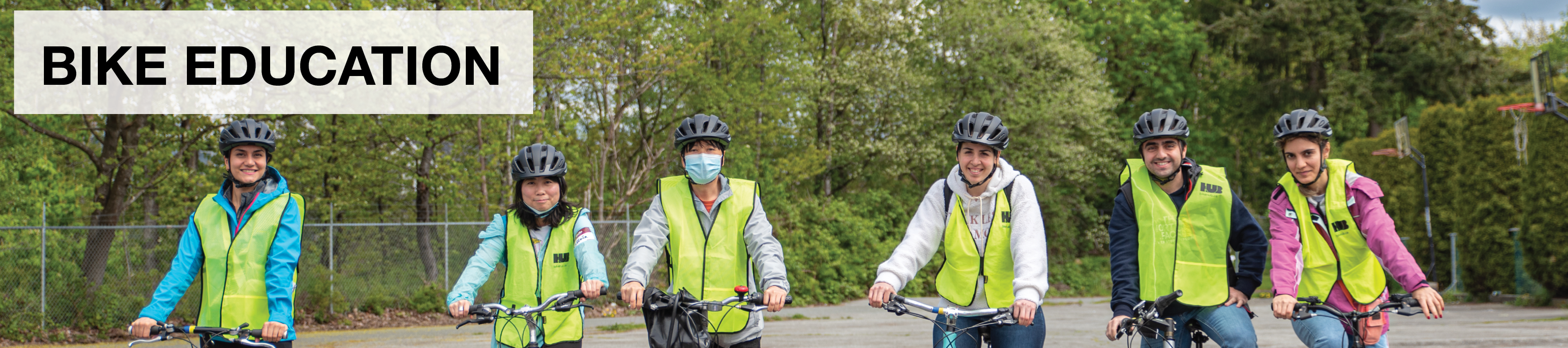 Bike Education. A group of adults wearing yellow vests stand on a gravel field with their bikes and smile.