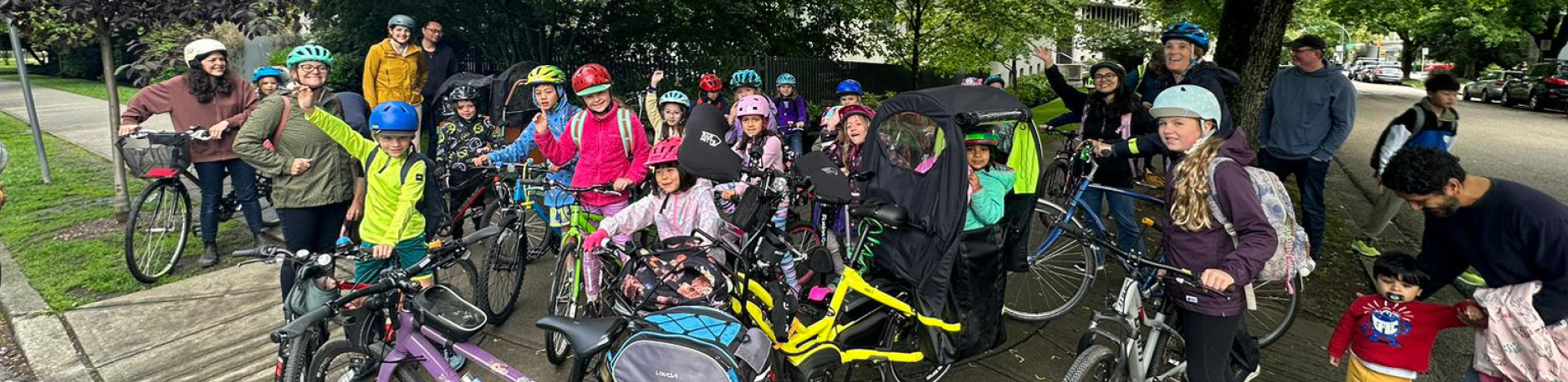 A group photo of elementary school-aged children roughly 7 years of age standing with their bikes and scooters on school grounds.