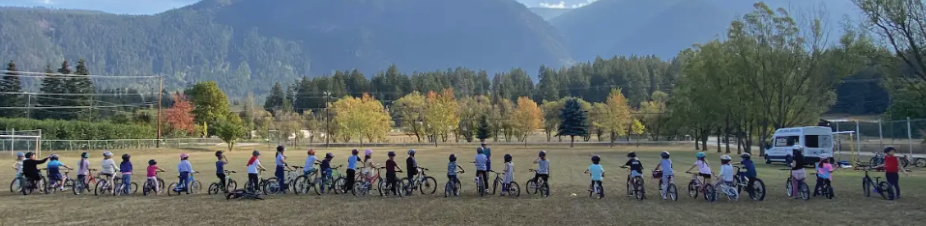 A large group of students stand in a field with their bikes in a row.