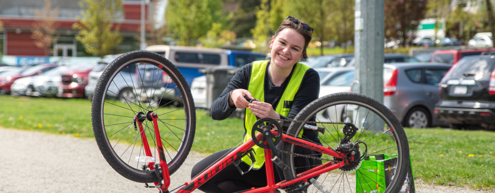 A bike education instructor kneels down and is changing the pedal of a bike that is flipped upside down. She smiles at the camera.