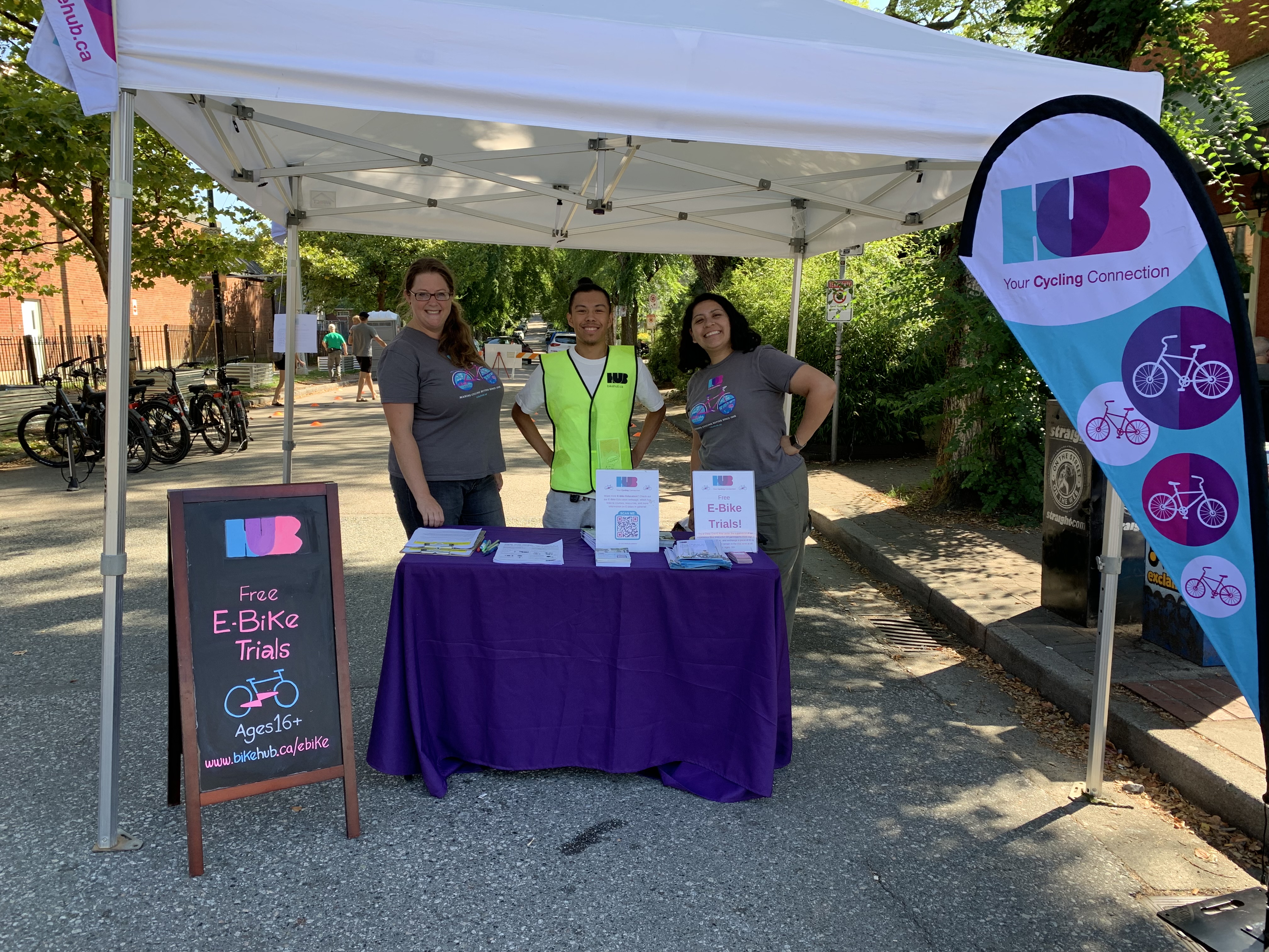 Three HUB Cycling staff members stand behind a booth at Car Free Days.