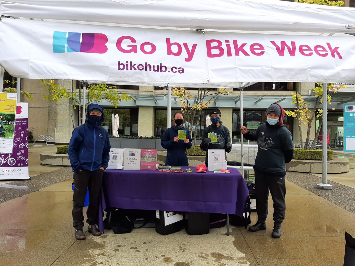 Lucy and Ulyana stand with two volunteers at a Knowledge HUB station in Vancouver