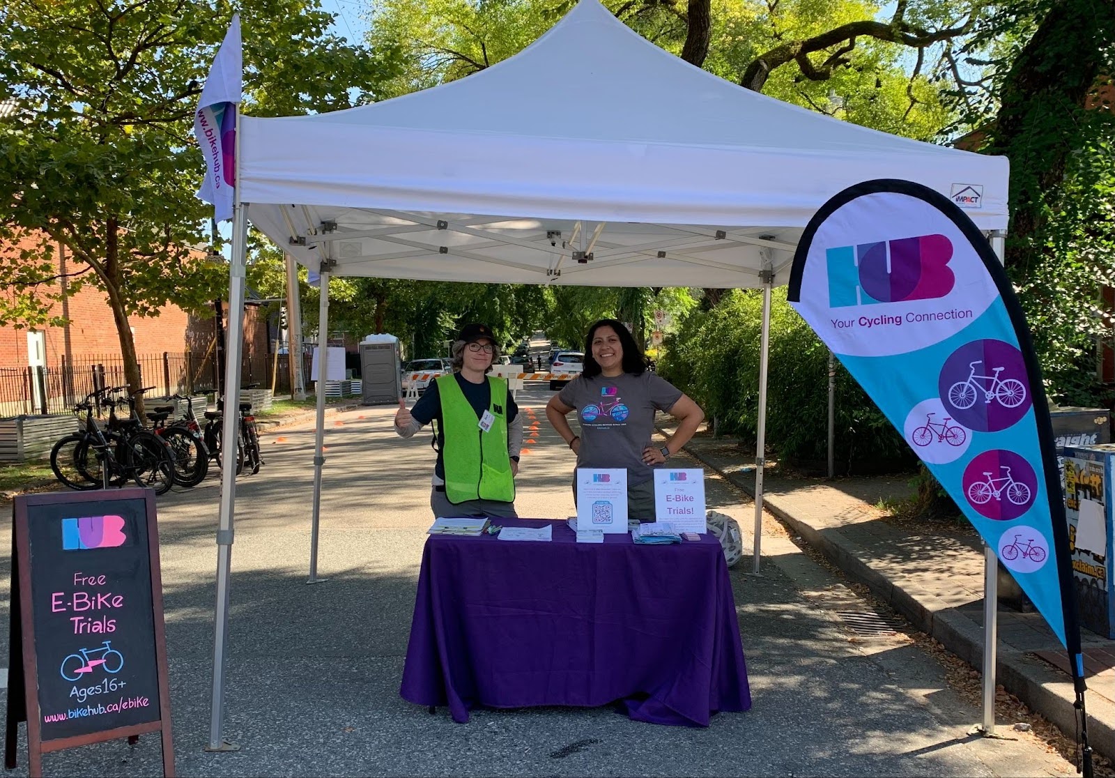 Two people stand at a booth for the E-bike Trial event at Car Free Day in Vancouver