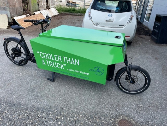 A photo of Chris' e-cargo bike. The bike is green and has "COOLER THAN A TRUCK" written on the side.