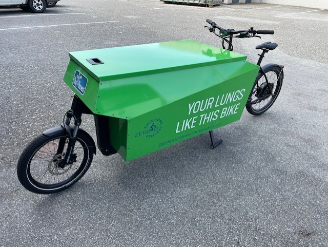 A photo of Chris' e-cargo bike. The bike is green and has "YOUR LUNGS LIKE THIS BIKE" written on the side.